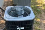Residential AC Maintenance in Norcross by The Air Company of GA. Technician using gauge manifold to check air conditioner unit pressure outdoors on grassy ground near red bucket.