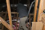 Commercial HVAC Repair in Atlanta 30324 by The Air Company of GA.  Worker wearing a hoodie and pants inspecting ductwork in a wooden attic space with insulation and pipes.