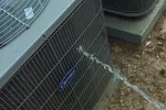 AC Repair and Maintenance in Smyrna 30080 by The Air Company of GA. Outdoor Carrier air conditioning unit being sprayed with water on dirt ground with leaves.