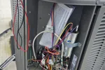 Commercial HVAC Repair in Atlanta Decatur 30317 by The Air Company of GA.  Open HVAC unit showing internal wiring, circuit board, capacitor, and a multimeter on top with connected test leads.