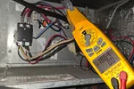 AC Heat Repair in Atlanta 30309 by The Air Company of GA.  Yellow clamp meter measuring voltage and current inside an electrical panel with multiple wires and components.