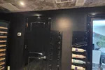 Wine Cellar Installation in Atlanta by The Air Company of GA.  Black wall with mounted wine racks holding bottles next to a closed black door and stone ceiling and floor.