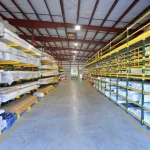 Spacious warehouse aisle with organized shelves stocked with lumber and construction materials under bright lighting.