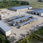 Aerial view of an industrial lumber yard with multiple storage buildings and stacks of wood materials.