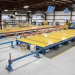 Large automated industrial machine with yellow and blue components inside a spacious manufacturing facility.