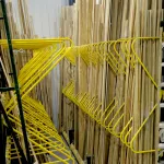 Yellow metal racks holding long wooden planks neatly organized in a warehouse aisle under bright lights