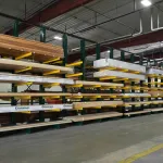 Warehouse interior with organized wooden lumber stacked on metal racks under industrial ceiling.