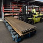 Worker operating forklift moving metal sheets in an industrial outdoor storage area with shelves.
