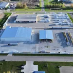 Aerial view of an industrial facility with large warehouses and organized storage areas in an urban setting.