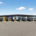 Outdoor covered storage racks holding various lumber and building materials under a clear blue sky.