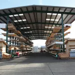 Outdoor lumber storage with metal roof and stacked wooden planks on shelves in a lumberyard.