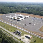 Aerial view of a large bus depot with multiple buses parked and surrounded by forest and roads.
