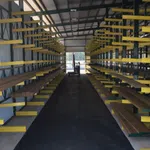 Warehouse aisle with yellow cantilever racks storing wooden planks inside a covered industrial building.