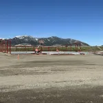 Construction site with red steel framework being erected against a mountain backdrop under clear blue sky