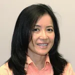 Portrait of a smiling woman with straight black hair wearing a peach collared shirt against a plain background