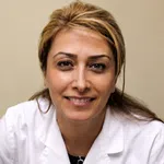 Smiling female healthcare professional wearing a white coat with a cute teddy bear patch on a beige background