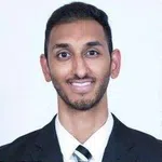 Smiling young man wearing a black suit, white shirt, and striped tie against a plain white background