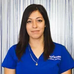 Woman wearing blue Burleson pediatric dentistry uniform against striped background smiling gently