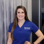 Smiling woman in blue Burleson pediatric dentistry scrubs standing with hand on hip against striped background