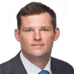 Professional headshot of a man in a suit and blue tie against a white background