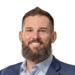 Smiling bearded man in a blue checkered blazer and patterned shirt on a white background