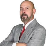 Confident middle-aged man with beard in gray checkered suit and red tie posing with arms crossed