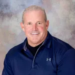 Smiling middle-aged man wearing a navy blue Under Armour polo shirt against a neutral backdrop