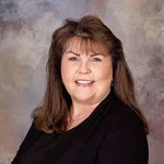 Smiling woman with shoulder-length brown hair wearing black clothing against a neutral background.