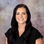 Smiling woman with long black hair and tattoos wearing a black shirt against a neutral background