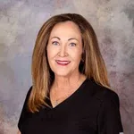 Smiling woman with long brown hair wearing a black shirt against a soft gray background