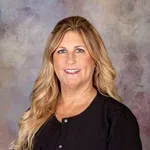 Smiling woman with long blonde hair wearing a black top against a blurred neutral background.