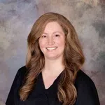 Smiling woman with long wavy hair wearing black medical scrubs against a neutral backdrop