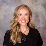 Smiling woman with long blonde hair wearing a black top against a neutral textured background