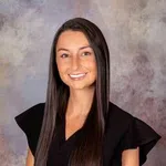 Smiling young woman with long straight brown hair wearing a black top against a textured gray background