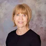 Smiling middle-aged woman with short blonde hair wearing a black top against a muted textured background.