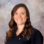 Smiling woman with long brown hair wearing black medical scrubs against a neutral backdrop