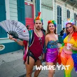 Four colorful, lively people in festive rainbow outfits posing on a New Orleans street during a celebration.