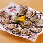 Grilled oysters on a white plate with lemon wedges, served on branded paper from Drago's Seafood Restaurant.