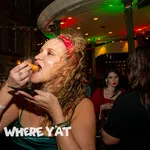 Woman in red headband eating fried food at lively nighttime party with people drinking and socializing.