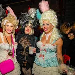 Four women in elaborate Halloween costumes with wigs and accessories at a festive party indoors.