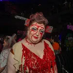 Woman in bloody costume with fake cleaver through head at a Halloween party with crowd in background