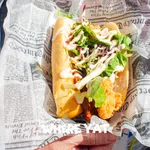 Fresh fried fish sandwich with lettuce and sauce served in newspaper-style wrapping held by a person.