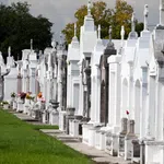 Row of white and gray above-ground tombs with flowers in a cemetery on a sunny day.
