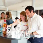 People enjoying drinks and socializing around a modern bar counter with bottles and glasses.