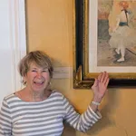 Smiling elderly woman pointing at framed impressionist painting of ballerina in museum setting
