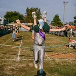 Person in eagle costume winning a race while carrying another runner across the finish line at outdoor event.
