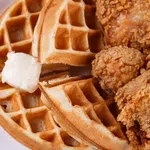 Crispy fried chicken pieces served with golden waffles and a dollop of melting butter on a white plate.