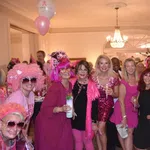 Group of women dressed in pink and black at an indoor party with balloons and drinks celebrating together.