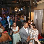 Crowded lively indoor party with guests socializing, dressed in formal and cocktail attire under chandeliers.