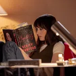 Woman reading the book Hospitality by Verity Crawford in a cozy, warmly lit room with a table lamp.